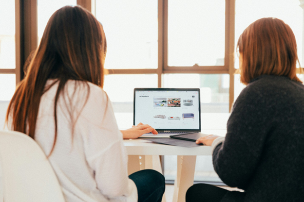 Two employees surfing colleges in Mississippi with a human resources degree on a laptop.